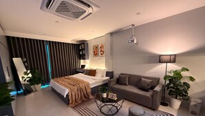 Quarto moderno com cama, mesa de cabeceira, abajur e uma grande janela com cortinas.