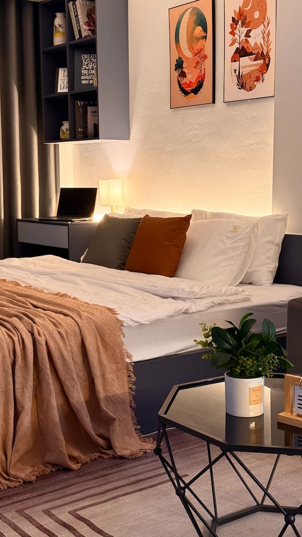 A modern bedroom with a bed, bedside tables, a desk, and a potted plant.
