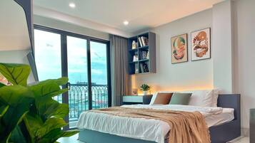A modern bedroom with a large bed, a nightstand, a bookshelf, and a view of the city through large windows.