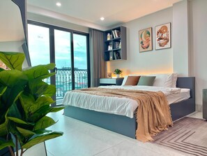 A modern bedroom with a large bed, a nightstand, a bookshelf, and a view of the city through large windows.