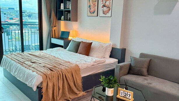 Um quarto moderno com uma cama, um sofá, uma mesinha com uma planta e vista para a cidade através de uma grande janela.