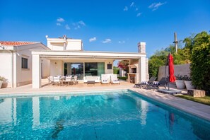 Ein modernes Haus mit Swimmingpool, Sitzgelegenheiten im Freien und einer überdachten Terrasse.