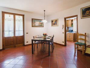 A dining area with a table set for four, a kitchen visible through an open door, and a chair with a cushion. - Casa Lulù by Interhome (Camaiore)