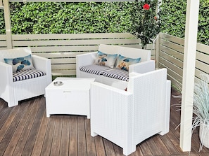 Ein Patio mit weißen Korbmöbeln, darunter zwei Stühle und ein kleiner Tisch.