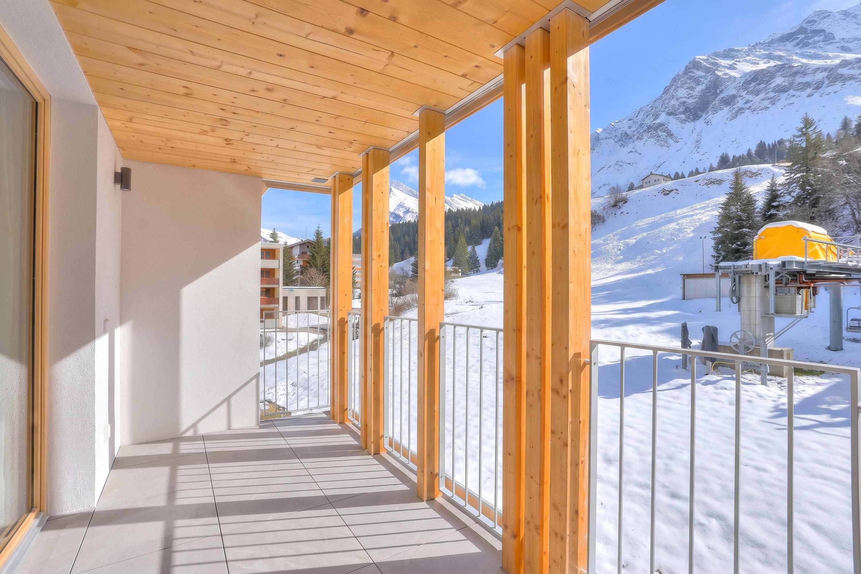 A balcony with wooden railings, a tiled floor, and a view of a snowy mountain landscape.