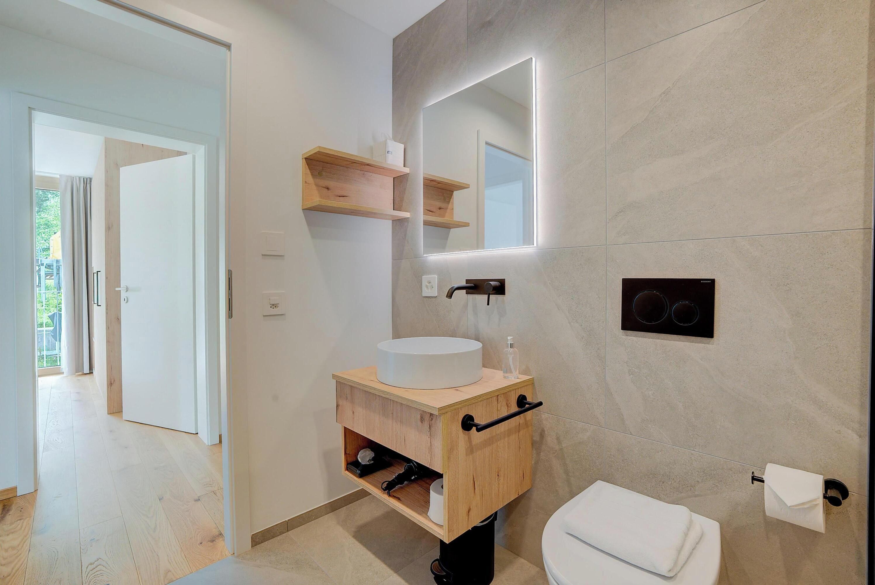 A modern bathroom with a wooden vanity, a round sink, a mirror, and a toilet.