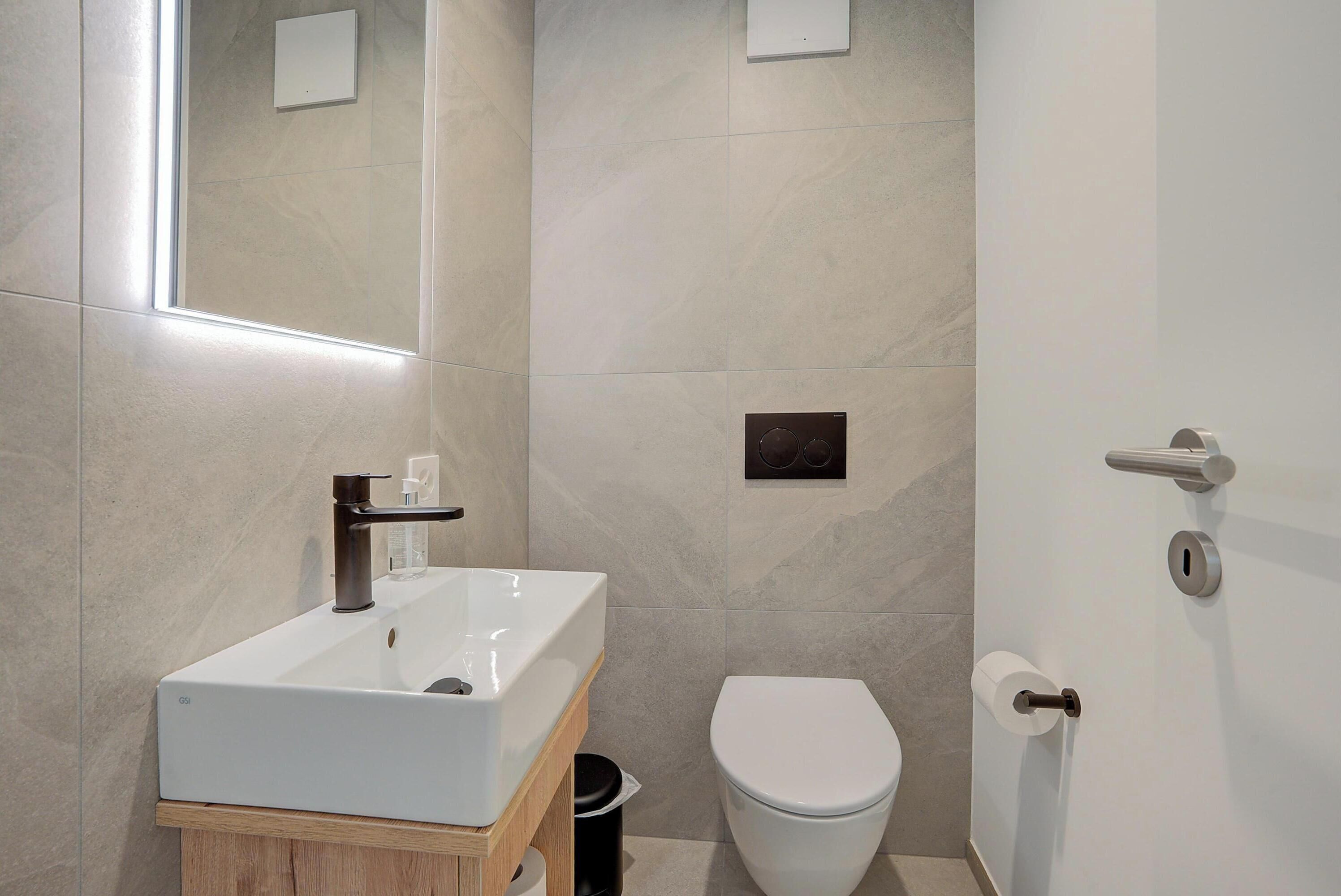 A modern bathroom with a white sink, a toilet, and a mirror.