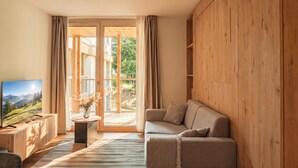 A modern living room with a wooden floor, a sofa, a TV, and a view of a balcony with a wooden railing. - Residenza Castanea 208 Modern Alpine Stay in San Bernardino | Ski, Hiking & Nature, San Bernardino, Switzerland (San Bernardino)