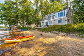 A lakeside cabin with a dock, kayaks, and a fire pit.