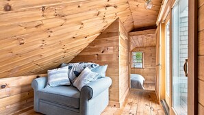 Un dormitorio de ático acogedor con techo de madera, un sofá gris con cojines y una ventana con persianas.