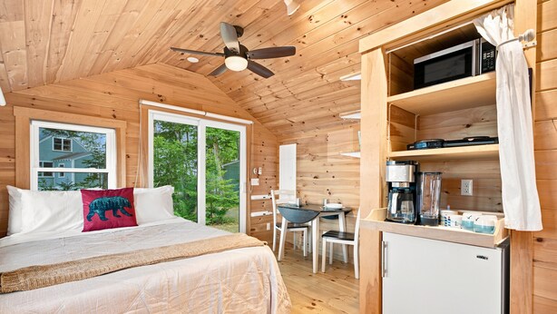 Interior de una cabaña de madera con una cama, comedor, kitchenette y ventilador de techo.