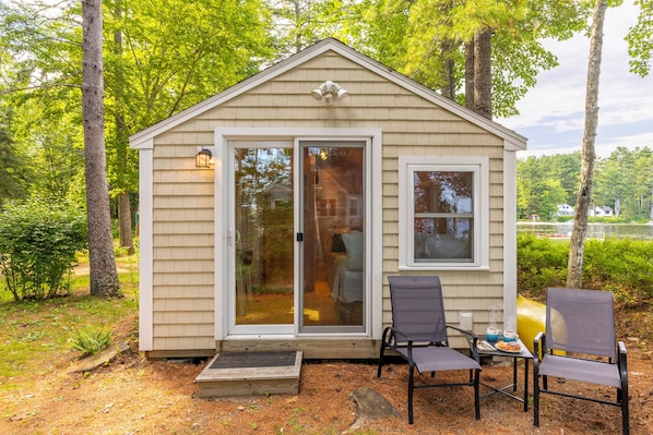 A small cabin with a sliding glass door, a porch with two chairs, and a table with a cup and a plate.