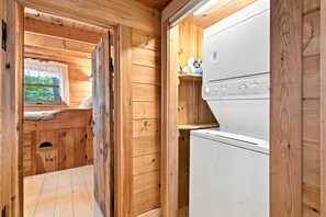 A wooden cabin interior with a bed, a window with a curtain, and a white appliance. - Rare 4-bed, 3-full bath Cottage & Tiny Home w/ Private Beach & Dock (Damariscotta)