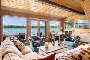 A cabin with a wooden interior, large windows, a dining area, and a view of a lake. - Rare 4-bed, 3-full bath Cottage & Tiny Home w/ Private Beach & Dock (Damariscotta)