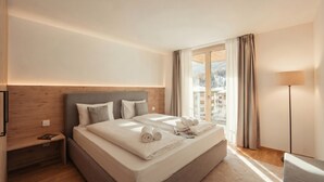 Quarto de hotel com uma cama grande, uma mesa de cabeceira, uma luminária e vista para uma paisagem nevada através da janela.