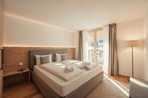 Ein Hotelzimmer mit einem großen Bett, einem Nachttisch, einer Lampe und Blick auf eine verschneite Landschaft durch ein Fenster.