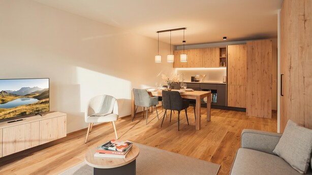 Uma sala de estar moderna com uma televisão de tela plana, um sofá, uma mesa de centro com livros e uma área de jantar com mesa e cadeiras.