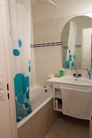 Ein Badezimmer mit einer Badewanne, einem Waschbecken, einem Spiegel und einem Duschvorhang mit blauem Muster.