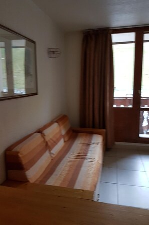 Una habitación con un banco de madera, un cuadro en la pared y un ventanal con cortinas.
