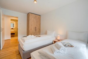 Habitación de hotel con dos camas, un armario de madera, una mesita de noche con lámpara y una revista sobre la cama.