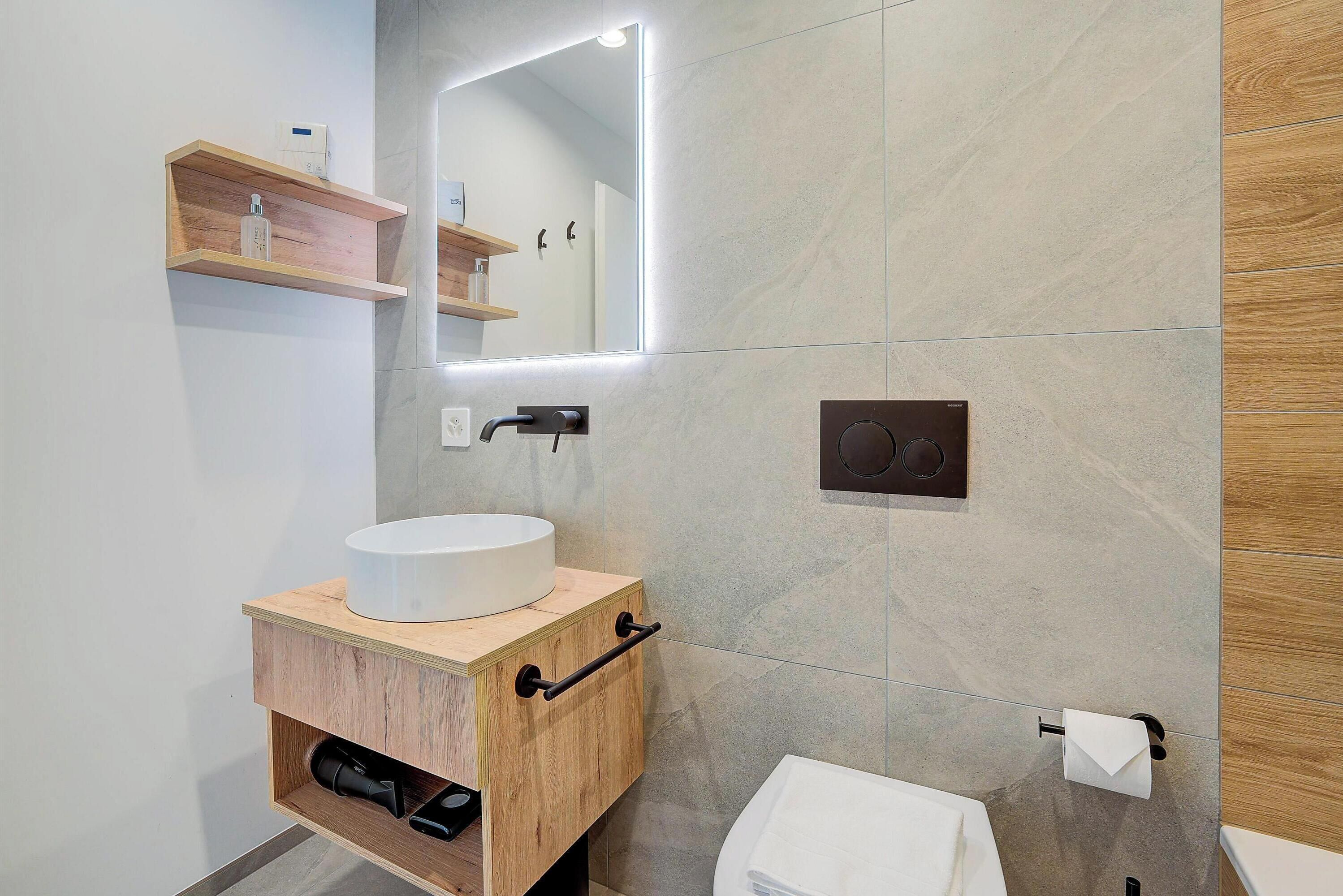 Ein modernes Badezimmer mit einem Holzkosmetikschrank, einem runden Waschbecken, einem Spiegel und einem Handtuchhalter.