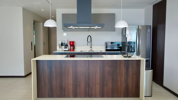 Een moderne keuken met een centraal eiland, roestvrijstalen apparatuur en hanglampen.