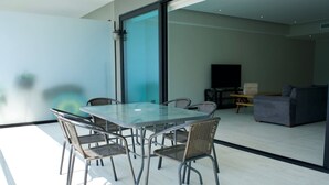 Een moderne woonkamer met een glazen eettafel, rieten stoelen, een bank en een televisie.