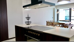 Een moderne keuken met een ingebouwde kookplaat, een zwart metalen mand met twee niveaus, en een eethoek met tafel en stoelen.