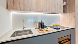 Een moderne keuken met een roestvrijstalen spoelbak, een waterkoker, een snijplank met groenten en houten keukenkastjes.