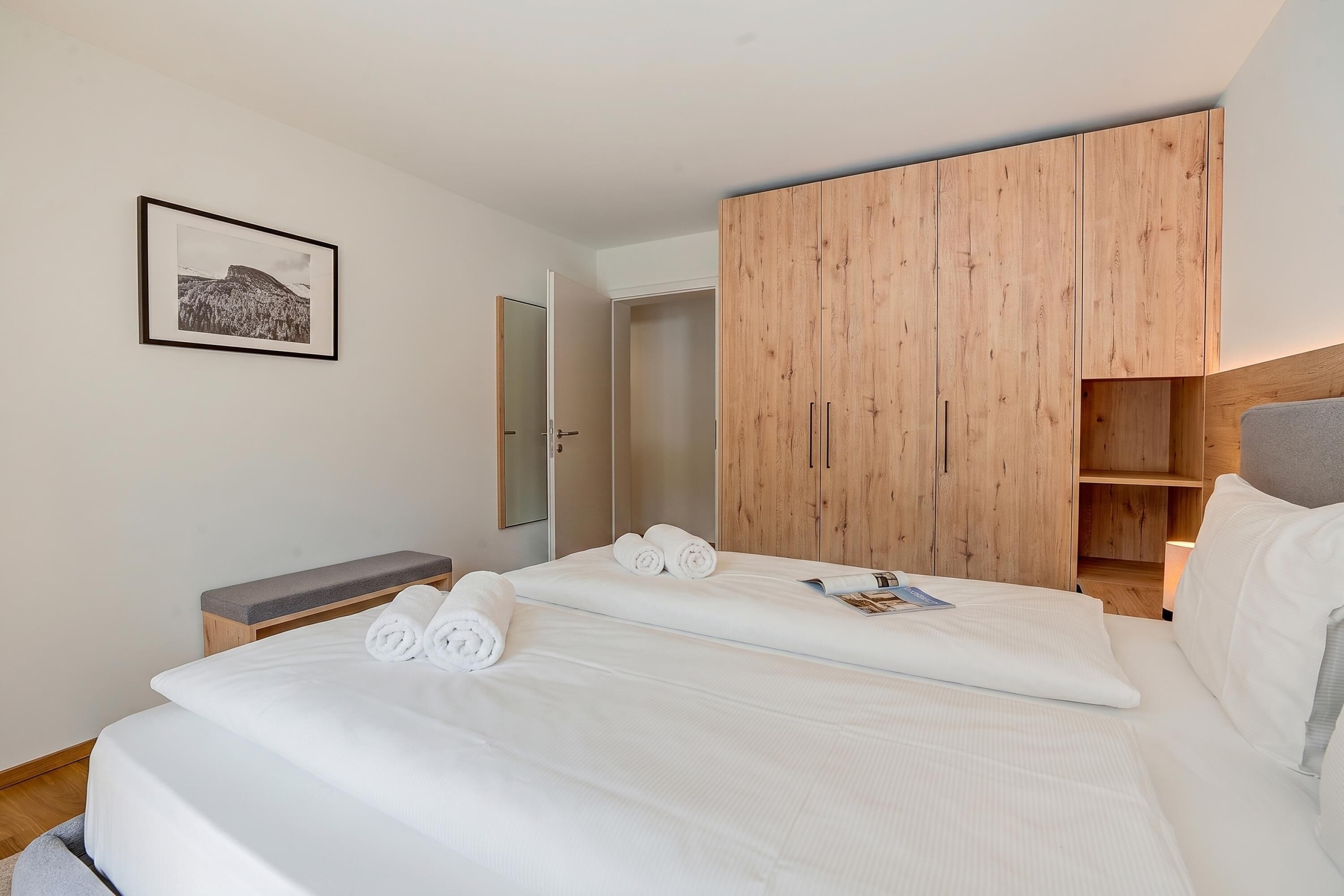 Une chambre d’hôtel avec un lit, une armoire en bois, un banc et un tableau encadré au mur.