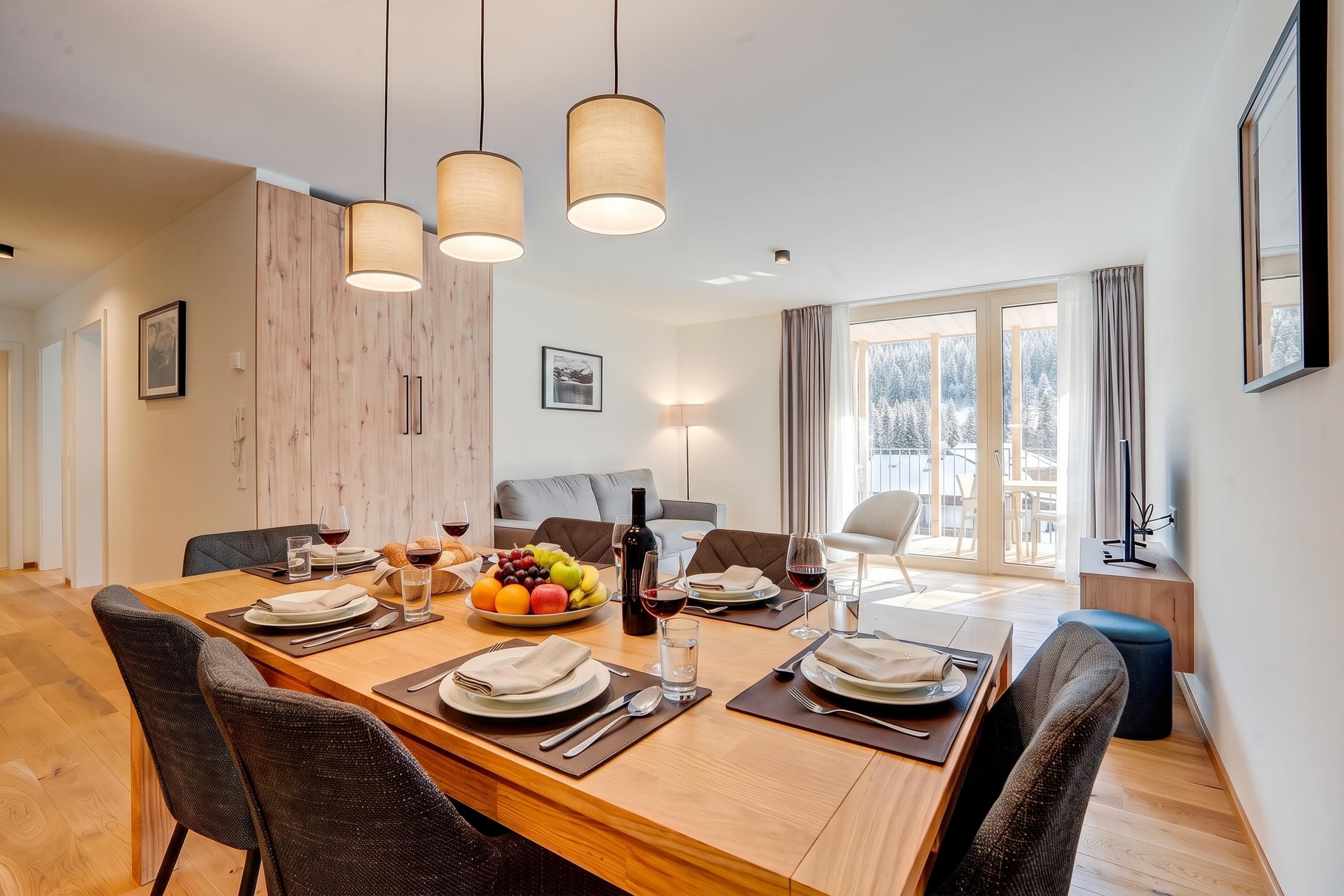Un comedor con una mesa de madera dispuesta para cuatro personas, rodeada de sillas, con vista a un paisaje nevado a través de amplios ventanales.