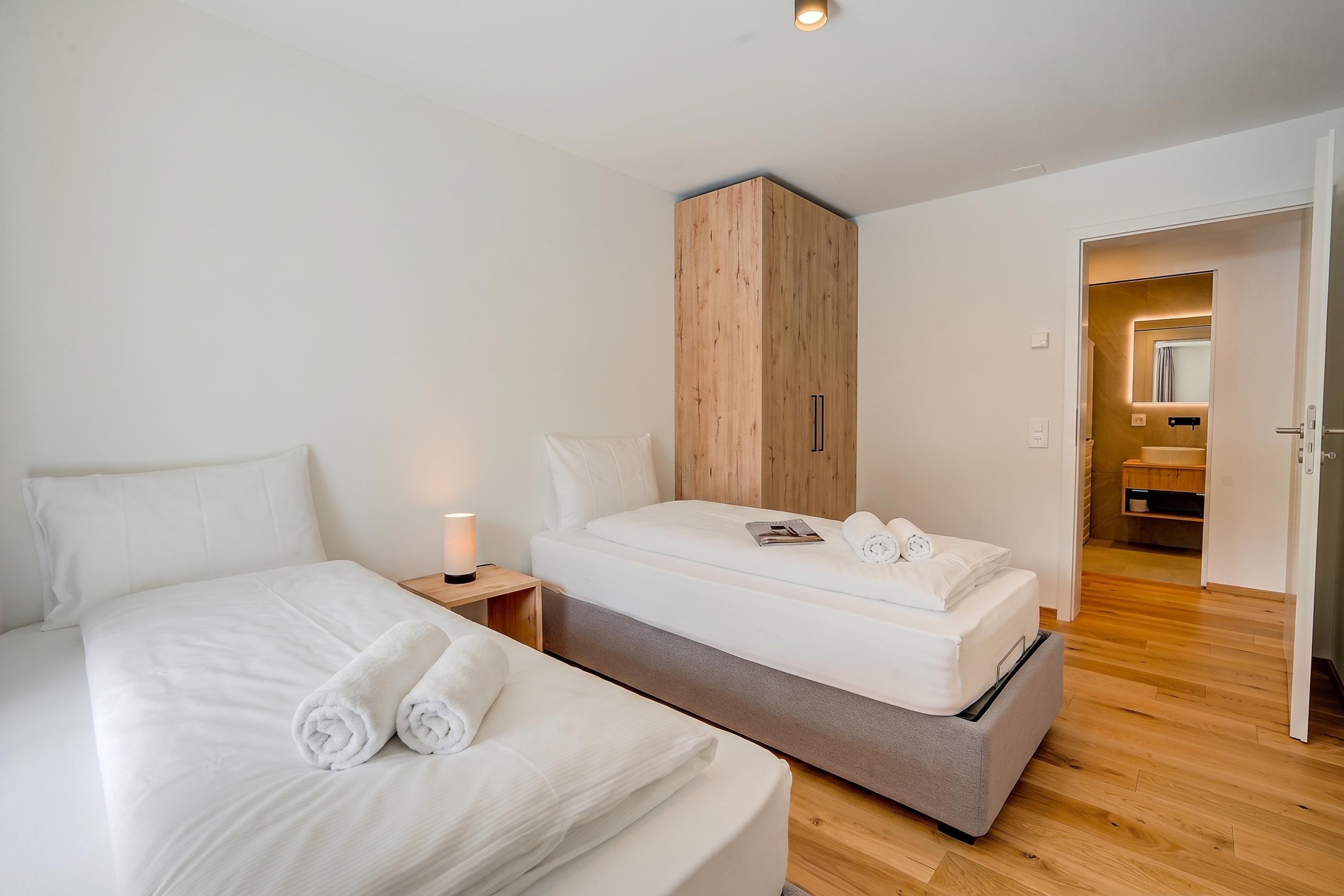 Ein Hotelzimmer mit Bett, Nachttisch, Kleiderschrank und angrenzendem Badezimmer, das durch eine geöffnete Tür sichtbar ist.
