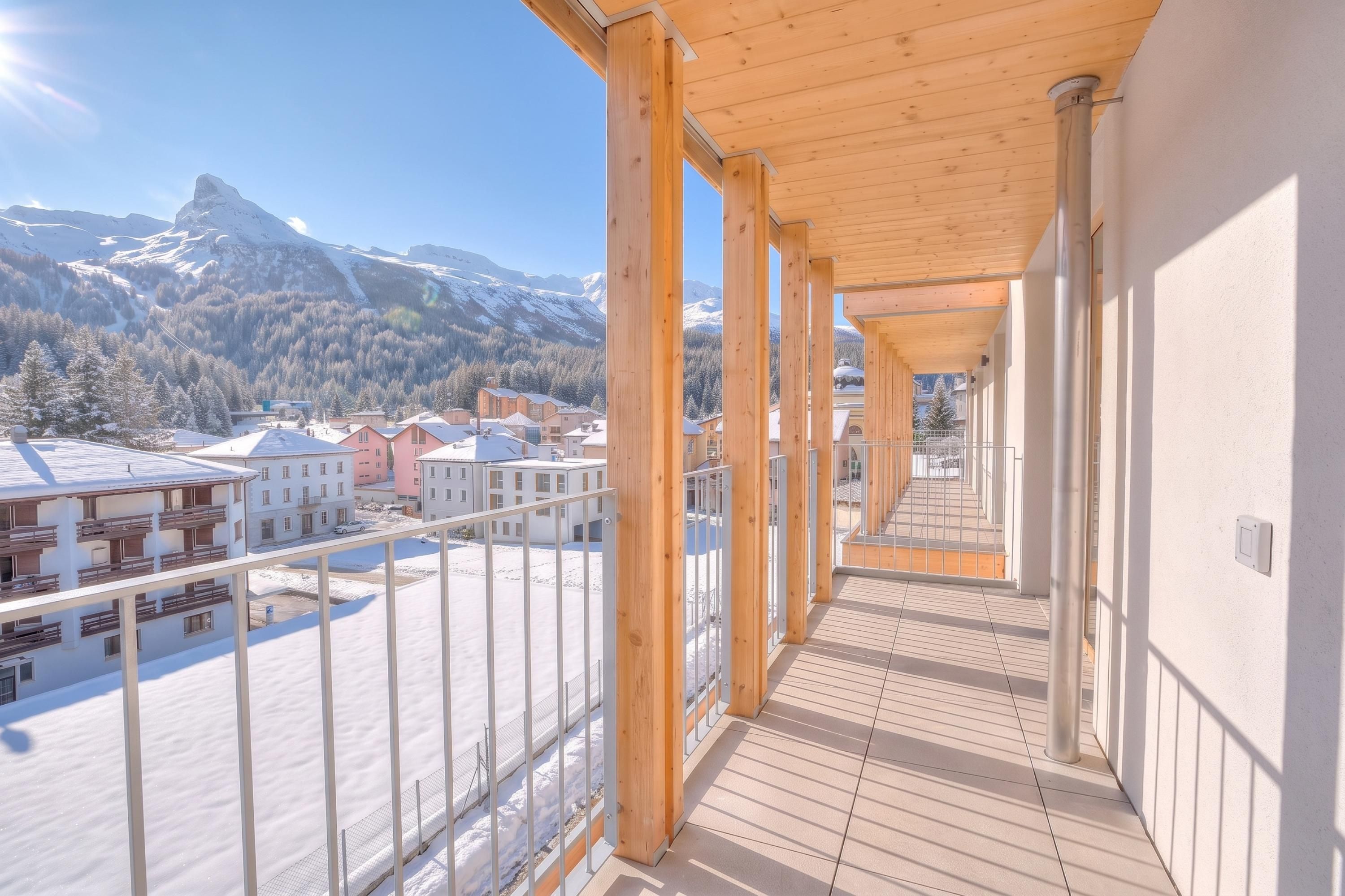 Passadís amb bigues de fusta i vista a muntanyes cobertes de neu i edificis.