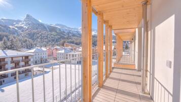 A corridor with wooden beams and a view of snow-covered mountains and buildings.