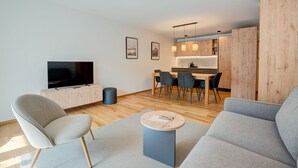 Een moderne woonkamer met een flatscreen televisie, grijze banken, een salontafel en een eethoek met een houten tafel en stoelen.