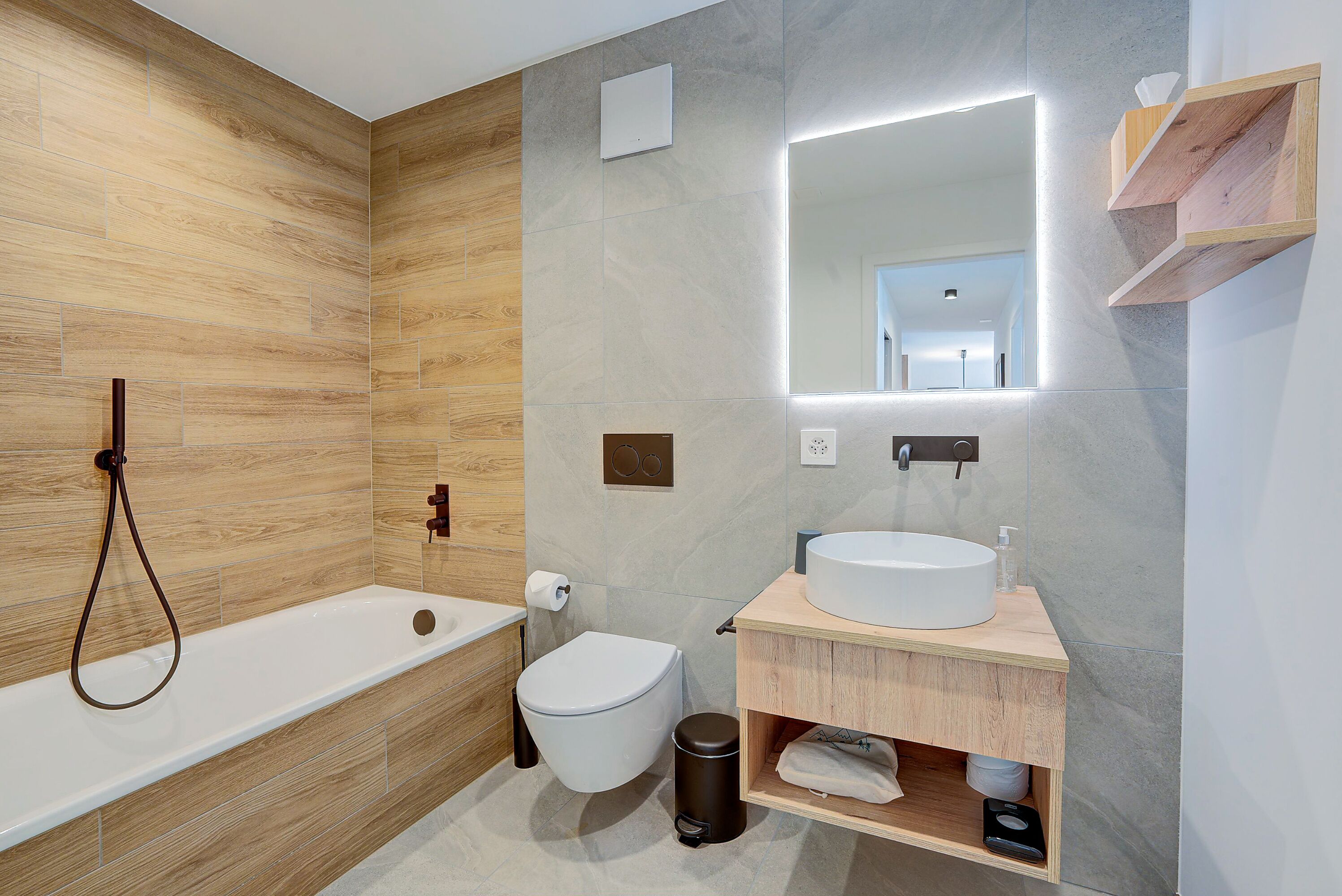 A modern bathroom with a wooden wall, a bathtub, a toilet, a sink, and a mirror.