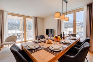 A dining room with a large table set for six, a television, and a view of a mountainous landscape. - Residenza Castanea 202 San Bernardino Alpine Apartments, San Bernardino, Switzerland (San Bernardino)