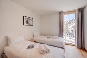 Ein Hotelzimmer mit zwei Betten, einem gerahmten Bild an der Wand, einem Fenster mit Vorhängen und Blick auf Gebäude.