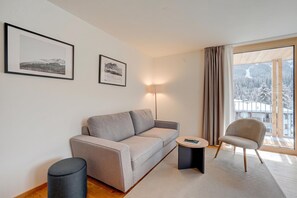 Ein modernes Wohnzimmer mit einer Couch, einem Beistelltisch, einem Sessel und einer Lampe. An der Wand hängen zwei gerahmte Bilder.