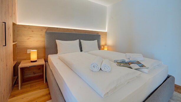 A neatly made bed with white linens and towels, a bedside table with a lamp, and a wooden headboard.