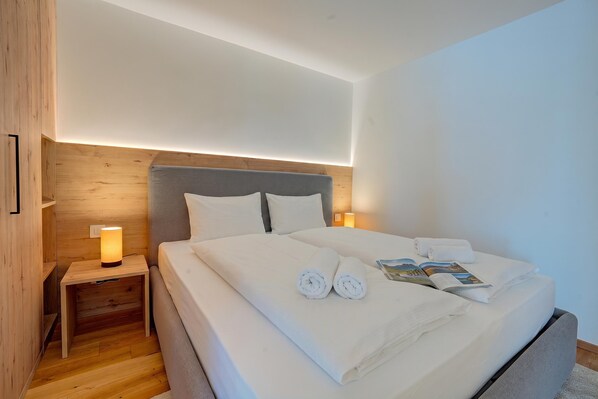 A neatly made bed with white linens and towels, a bedside table with a lamp, and a wooden headboard.