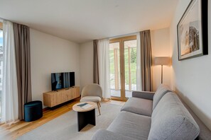 Un salon moderne avec un canapé, un téléviseur, une lampe et une vue à travers les portes vitrées.