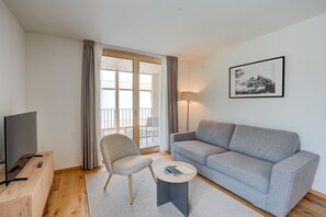 A modern living room with a grey sofa, a chair, a coffee table, a TV, and a framed picture on the wall.