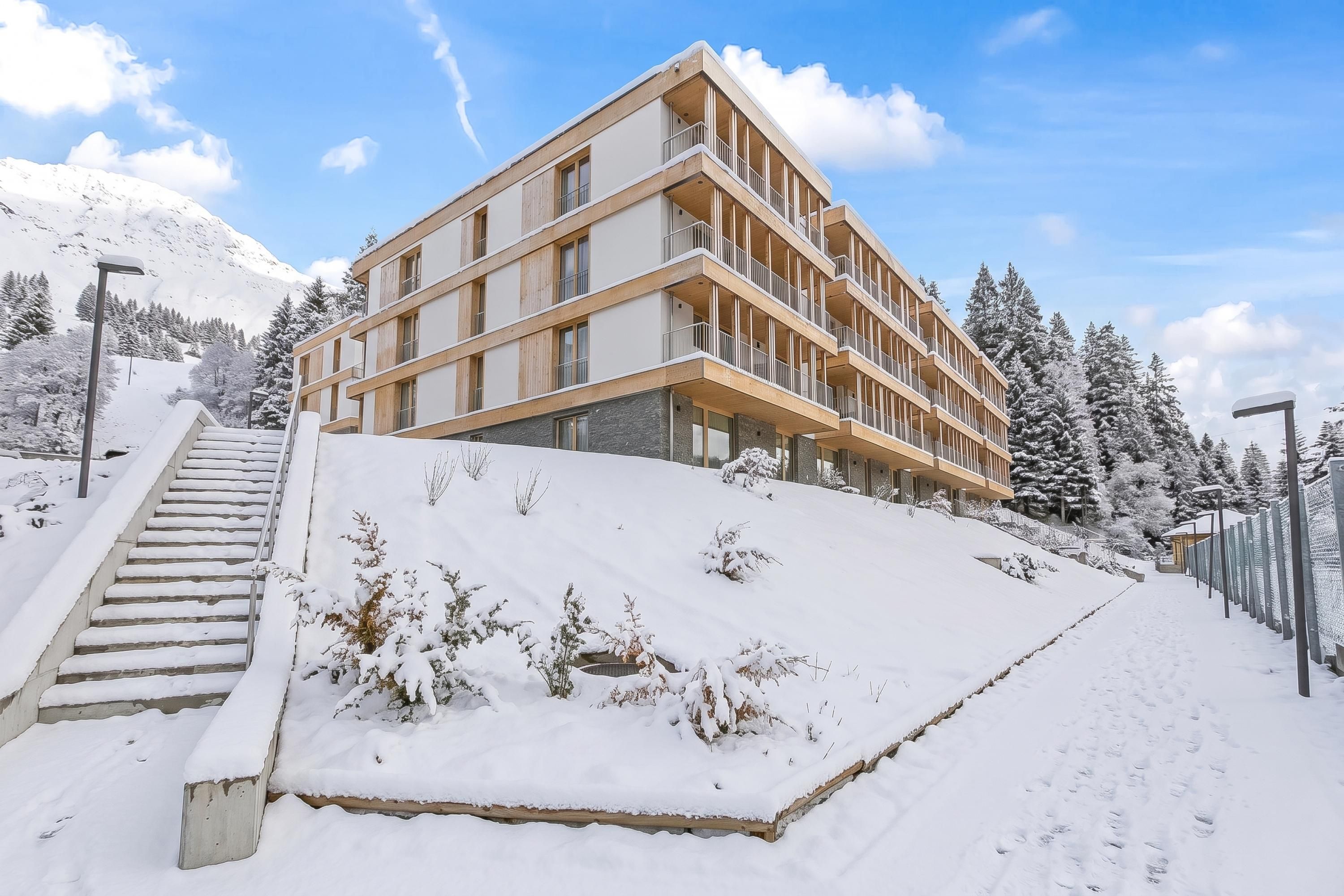 Een meerlaags hotel met een modern ontwerp, gelegen op een besneeuwde helling met een trap die naar de ingang leidt.
