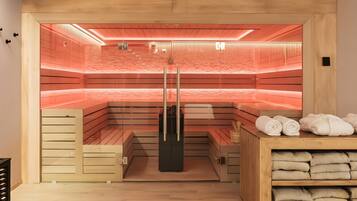 Una sauna con panche in legno, un recinto in vetro, un porta asciugamani e uno scaffale con asciugamani.