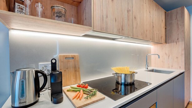Una cocina moderna con estufa integrada, hervidor, tabla de cortar con verduras y una olla de pasta.