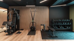 Un gimnasio con equipo de ejercicio, una banca y un estante con mancuernas.