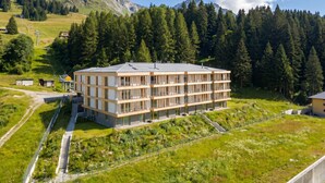 Ein mehrstöckiges Hotel mit flachem Dach, umgeben von üppiger grüner Landschaft und einem Wald.