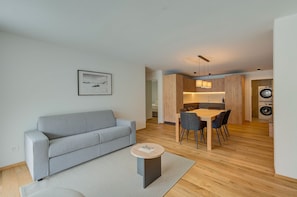 Una sala de estar moderna con un sofá gris, una mesa de comedor con sillas y una mesita redonda con un libro.