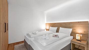 A modern bedroom with a wooden headboard, a bed with white linens, and a bedside table with a lamp.